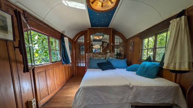 Un dormitorio con cama, paredes de madera, ventilador de techo y ventanas amplias.