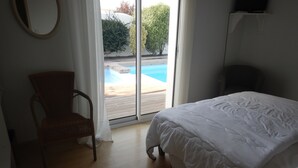 Une chambre avec un lit, une chaise et une vue sur une piscine extérieure, visible à travers une porte vitrée.