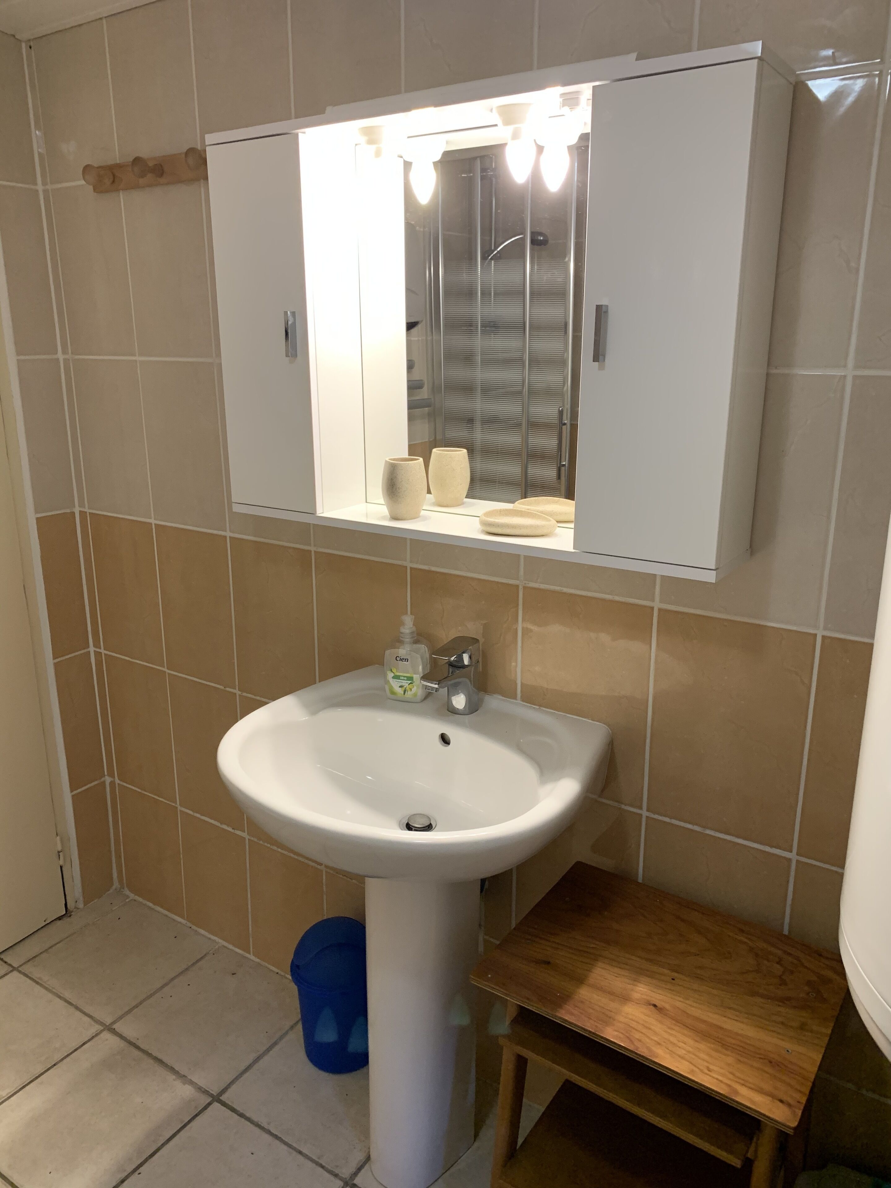 Un baño con un lavabo blanco, un espejo encima y un taburete de madera.