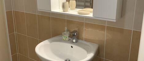 Un baño con un lavabo blanco, un espejo encima y un taburete de madera.