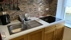 A kitchen with a stainless steel sink, a kettle, a coffee maker, and a stove.