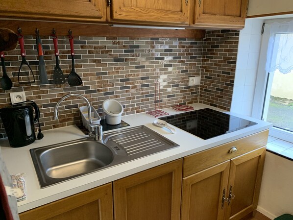A kitchen with a stainless steel sink, a kettle, a coffee maker, and a stove.