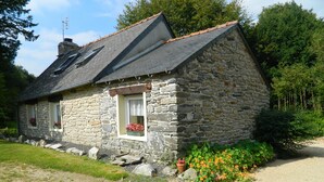 A stone house with a sloped roof, a small porch, and a gravel driveway.