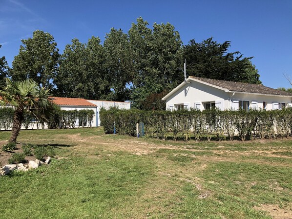 A white building with a tiled roof, surrounded by a well-maintained lawn and dense trees.