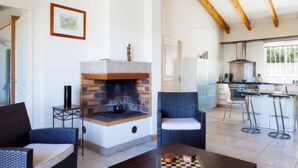 A living area with a fireplace, wicker furniture, a kitchen with bar stools, and a checkered game board. - Villa, pool sea view  (Belvédère-Campomoro)