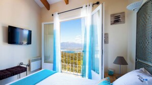 A bedroom with a bed, a TV, a balcony with a view, and a window with curtains. - Villa, pool sea view  (Belvédère-Campomoro)