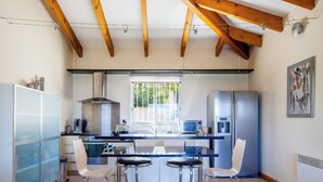 A modern kitchen with a central island, bar stools, a refrigerator, and a window with a view of greenery. - Villa, pool sea view  (Belvédère-Campomoro)