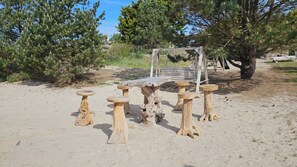 A rustic outdoor seating area with a wooden bench and stools, surrounded by trees and a wooden pergola.