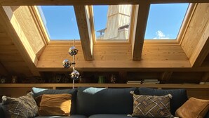 Ein Zimmer mit Holzbalkendecke und Oberlichtern, einem blauen Sofa und einem Glastisch.