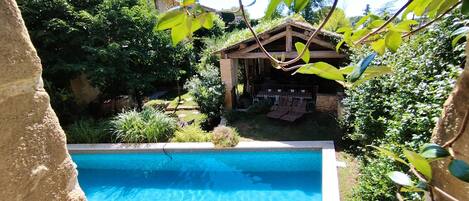 A swimming pool surrounded by lush greenery and a wooden structure with outdoor seating.
