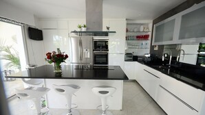 Una cocina moderna con una isla grande, electrodomésticos de acero inoxidable, armarios blancos y tres taburetes de bar.
