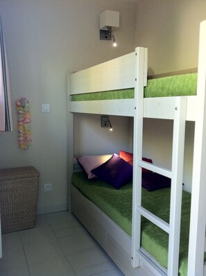 A bunk bed with a green mattress, a small bedside table, and a wall-mounted light fixture. - Apartment, facing the sea, near the beach, 6 people, 2 bedrooms (Le Lavandou)
