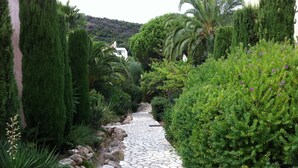 A stone pathway flanked by lush greenery and a mountain backdrop. - Apartment, facing the sea, near the beach, 6 people, 2 bedrooms (Le Lavandou)
