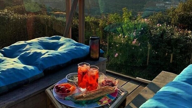 A wooden deck with a table set for a meal, a smartphone, and a view of a mountainous landscape.