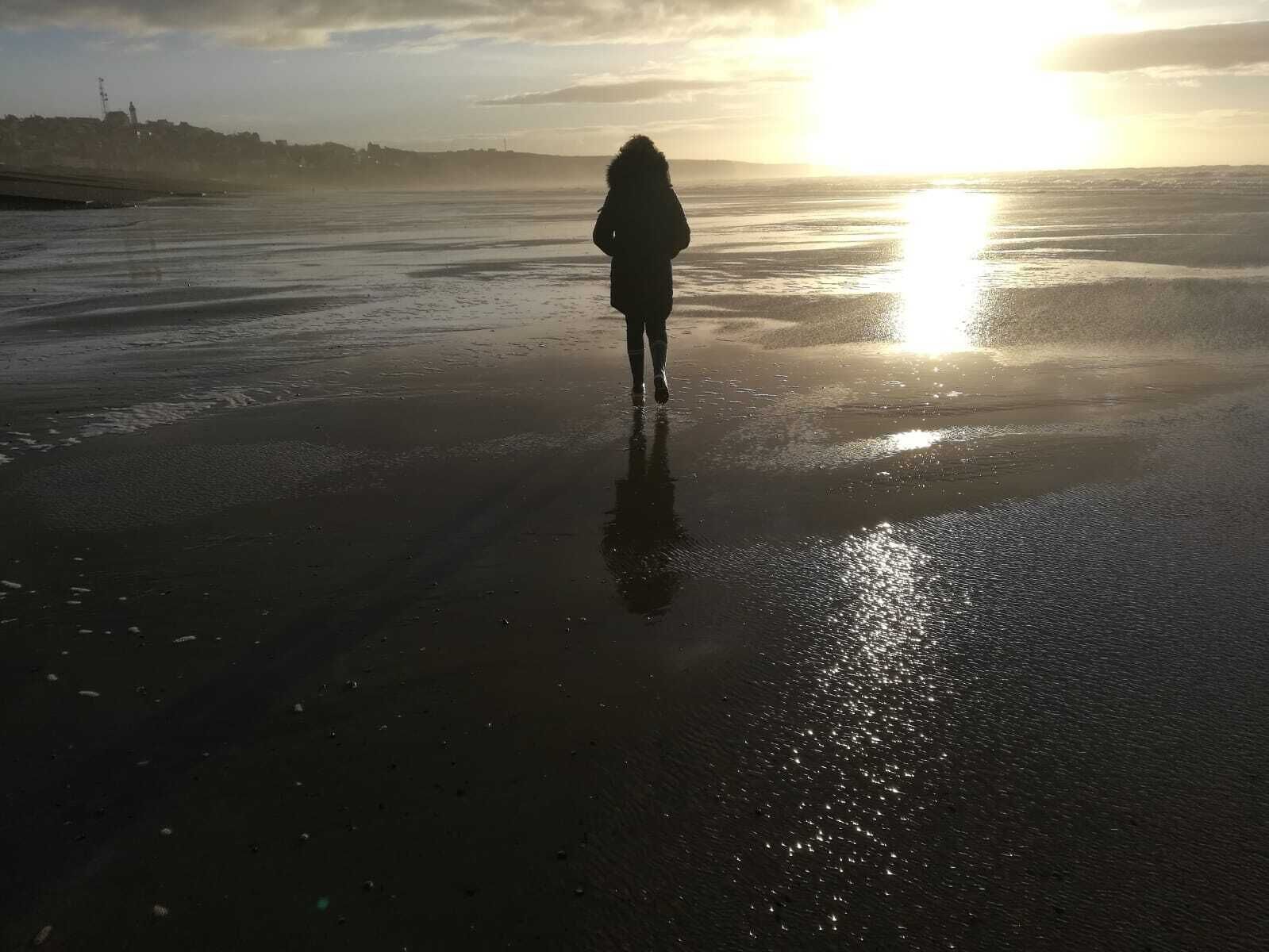 Une personne se promenant sur une plage mouillée au coucher du soleil.