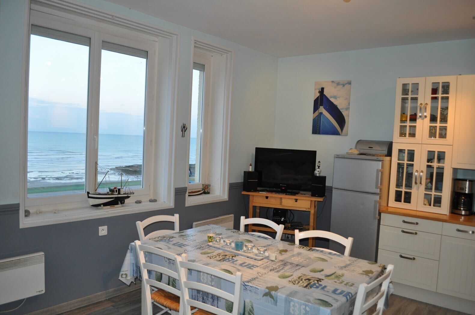 Une petite pièce agréable et chaleureuse, avec une table à manger, des chaises, un téléviseur et une vue sur la mer grâce à de grandes fenêtres.