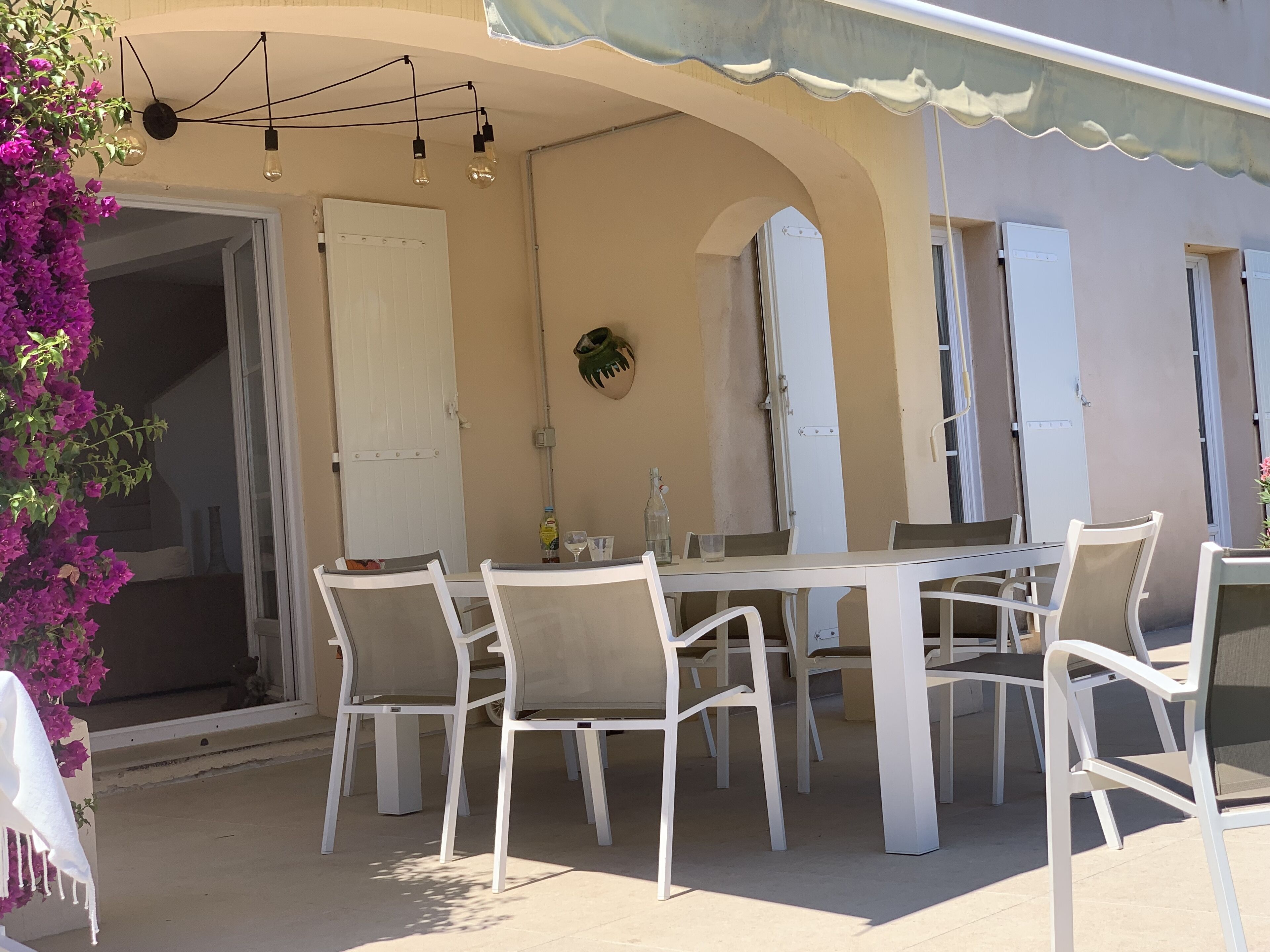 An outdoor dining area with a white table and chairs, a hanging light fixture, and a door.