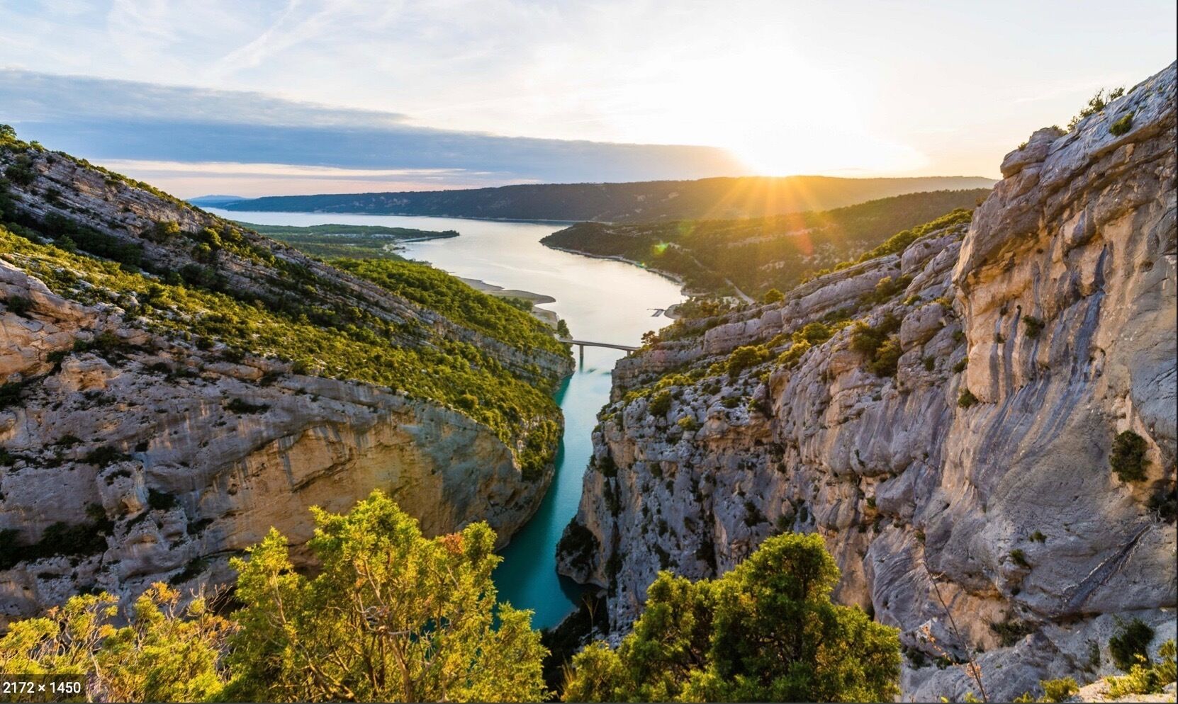 A gorge with a river, rocky cliffs, and greenery.