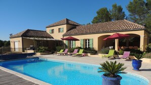 Une piscine entourée d’une terrasse en bois et de plantes en pot, avec des chaises longues et des parasols à proximité.