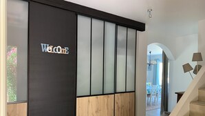 Un espace d’accueil moderne, agrémenté d’une enseigne « Bienvenue », d’une porte coulissante à panneaux dépolis et d’un escalier menant à un autre niveau.