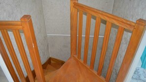 Une chaise en bois, dotée d’un dossier et d’accoudoirs, se trouve dans un coin de la pièce.