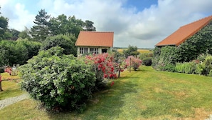 Ett hus med ett rött tegeltak, omgivet av frodig grönska och blommande buskar.