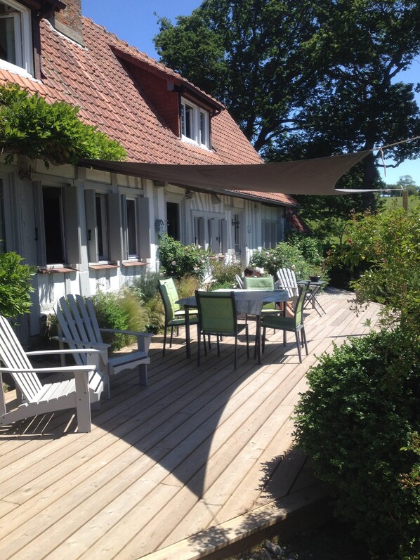 A wooden deck with outdoor furniture, a covered patio area, and a house with a red-tiled roof.