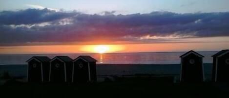 Un atardecer sobre el océano con cabañas de playa al frente.
