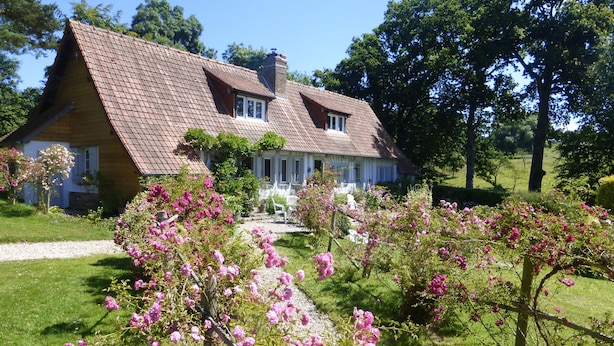 Ett traditionellt hus med ett sluttande tak, en veranda och en trädgård med blommande, rosa blommor.