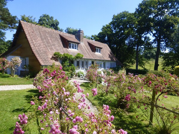 A traditional house with a sloped roof, a front porch, and a garden with blooming pink flowers.