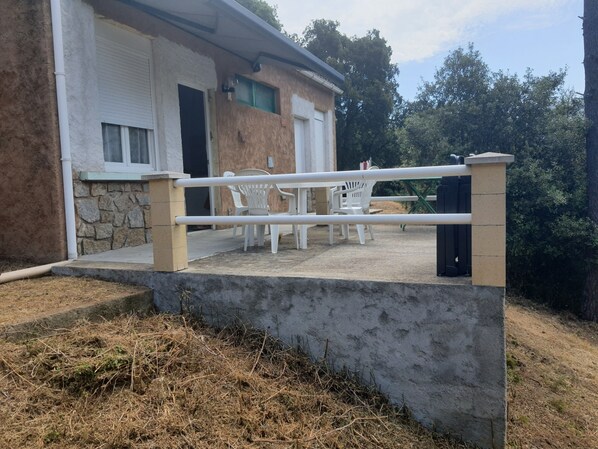 Una barrera de concreto con barandilla metálica, un muro de piedra y un edificio con fachada blanca y ventana verde.