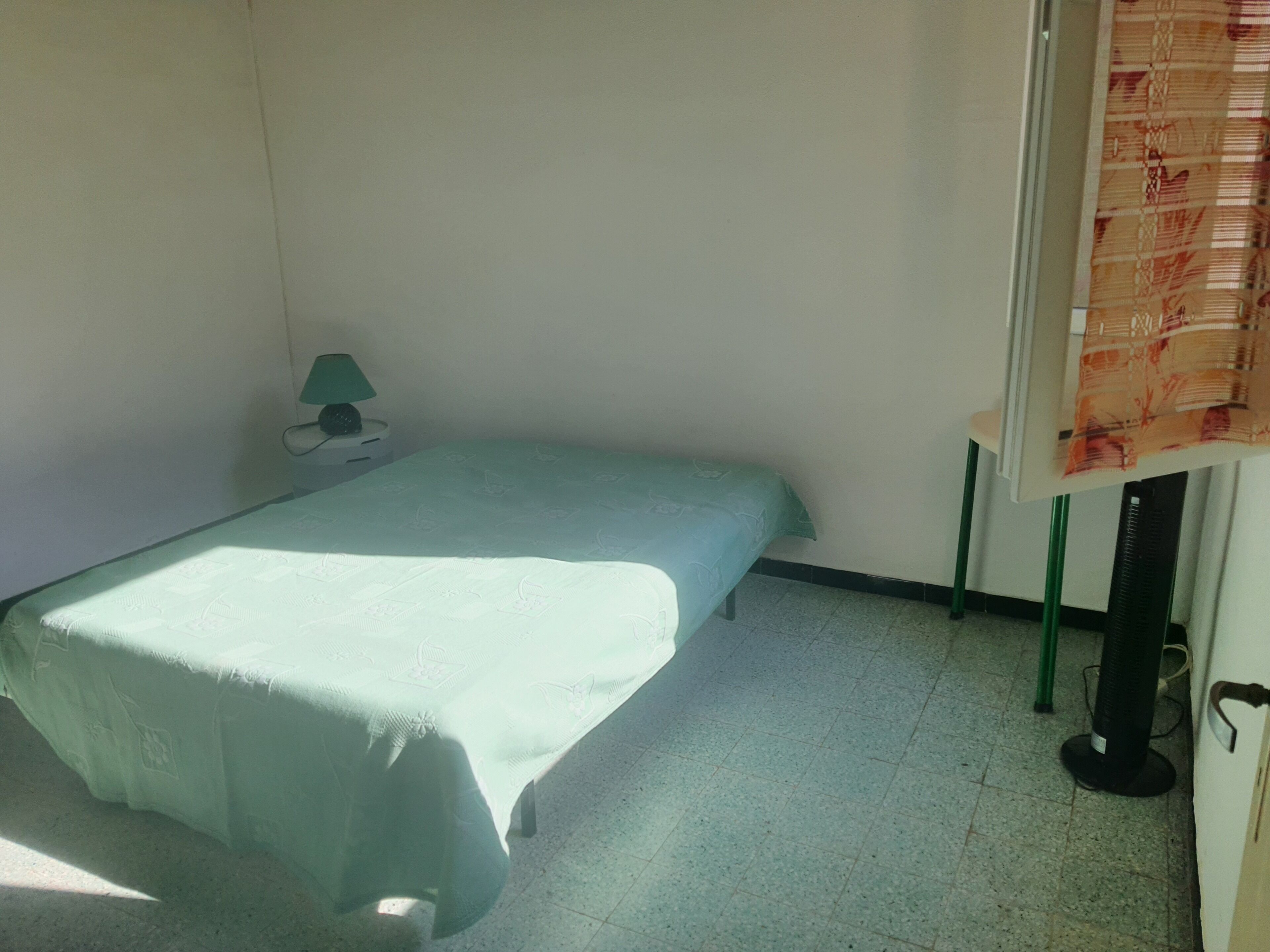A small, single-bed room with a bed, a nightstand, a lamp, and a radiator.