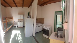 A compact kitchen with a refrigerator, stove, and a small dining area with a chair. - Mini-villa 300m beach. (Calcatoggio)