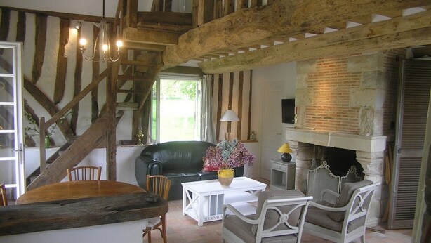Ein rustikales Interieur mit freiliegenden Holzbalken, einem Kamin, einer Essecke mit Tisch und Stühlen sowie einer Couch.
