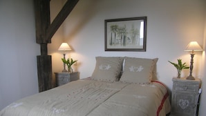 Ein Schlafzimmer mit einem großen Bett, zwei Nachttischen, zwei Wandlampen, einem gerahmten Bild über dem Bett und einer Holzbalkenkonstruktion.