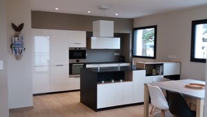 Une cuisine moderne avec des meubles blancs, un plan de travail noir et un four encastré. On y trouve également un coin repas avec une table blanche et des chaises noires.