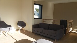Un salon moderne avec un canapé gris, un pouf assorti et une petite table d’appoint en bois.