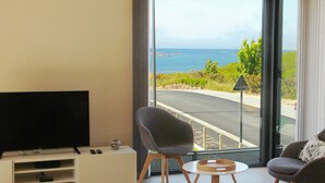 Une chambre avec une télévision, une chaise, une petite table et une vue sur la mer et la route.