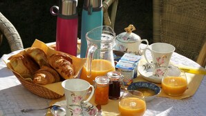 Desayuno con cruasanes, jugo y leche sobre una mesa al aire libre.