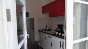 Una cocina compacta con armarios blancos, un refrigerador de acero inoxidable y un gabinete superior rojo.