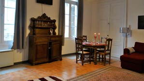 Una sala de estar con una mesa de comedor preparada para dos personas, un sofá rojo, un aparador de madera y un televisor en la pared.