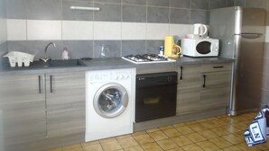 A modern kitchen with grey and white tiles, stainless steel appliances, a built-in washing machine, and a microwave.