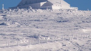 A large, white, single-story building with a sloped roof, surrounded by a snow-covered landscape and a clear blue sky.
