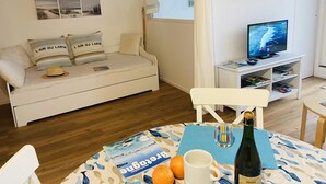 Ein gemütliches Wohnzimmer mit einer Couch, einem Fernseher und einem Tisch mit einer Flasche und Orangen.