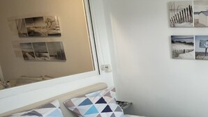 Ein Schlafzimmer mit Bett, Kissen und einem Hut auf dem Bett. An den Wänden hängen Bilder und das Fenster bietet einen Ausblick nach draußen.