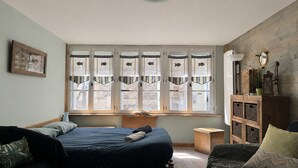 Un dormitorio con cama, ventana con cortinas decorativas, mesita de noche y un armario con espacio de almacenamiento.