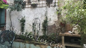Un espacio al aire libre rústico con un muro desgastado, una reja metálica y diversas plantas en macetas, además de una estatua.