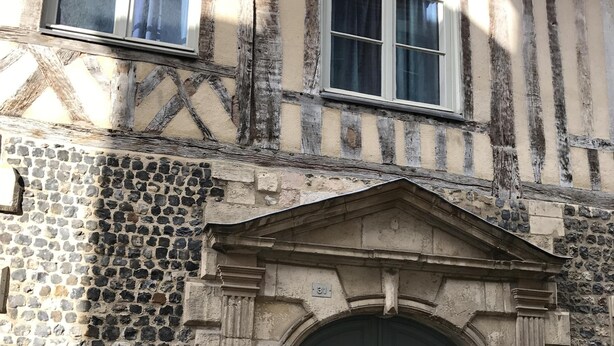 Un edificio histórico con fachada de piedra, una entrada abovedada grande y una ventana con diseño de cuadrícula.