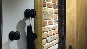 Una habitación con pared de ladrillo, puerta de madera y abrigo negro colgado de un perchero.