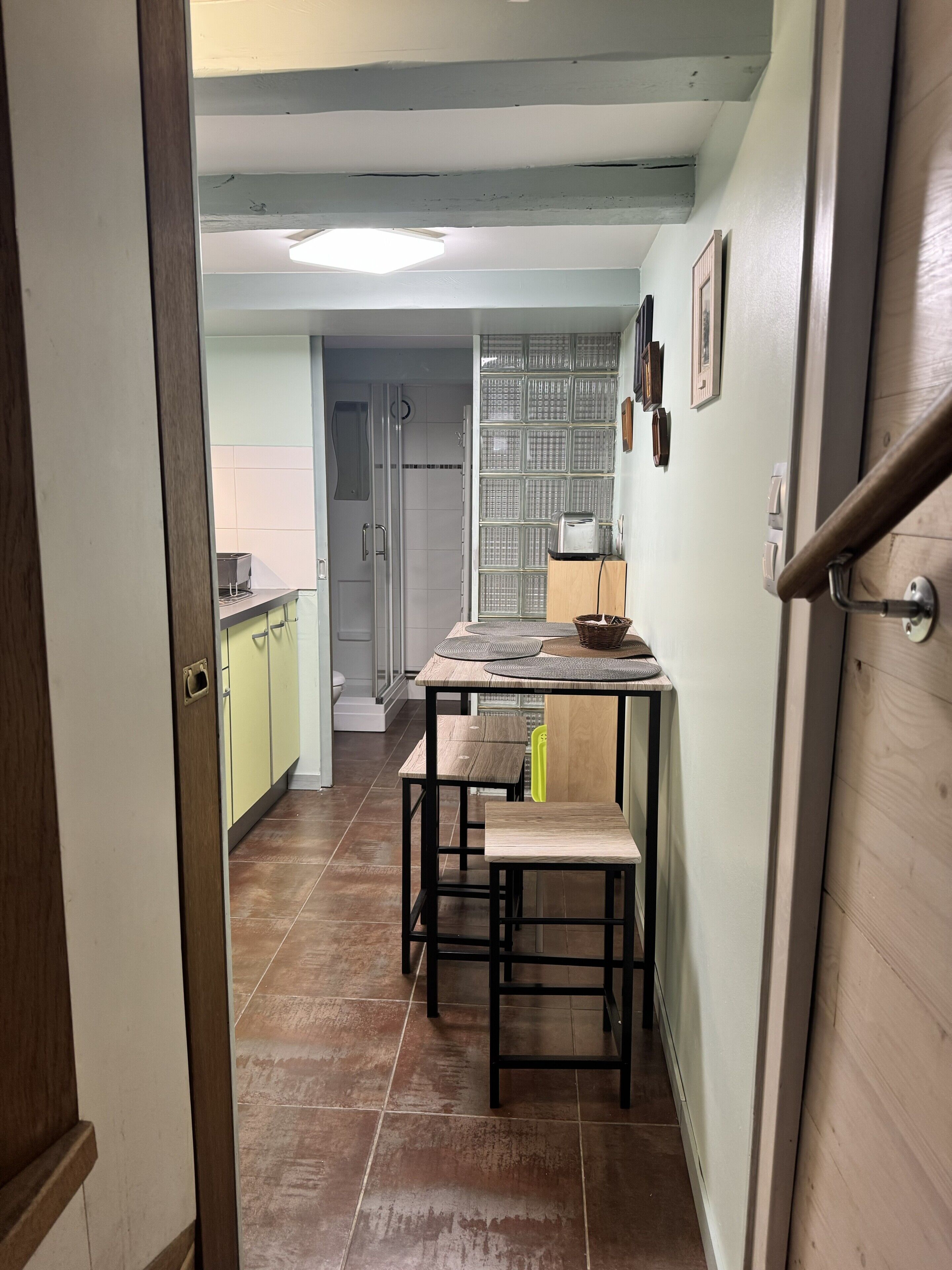 Un pasillo estrecho que da a una cocina con una mesa, sillas y un refrigerador.